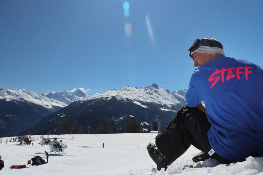 Un membre du staff assis dans la neige face aux montagnes